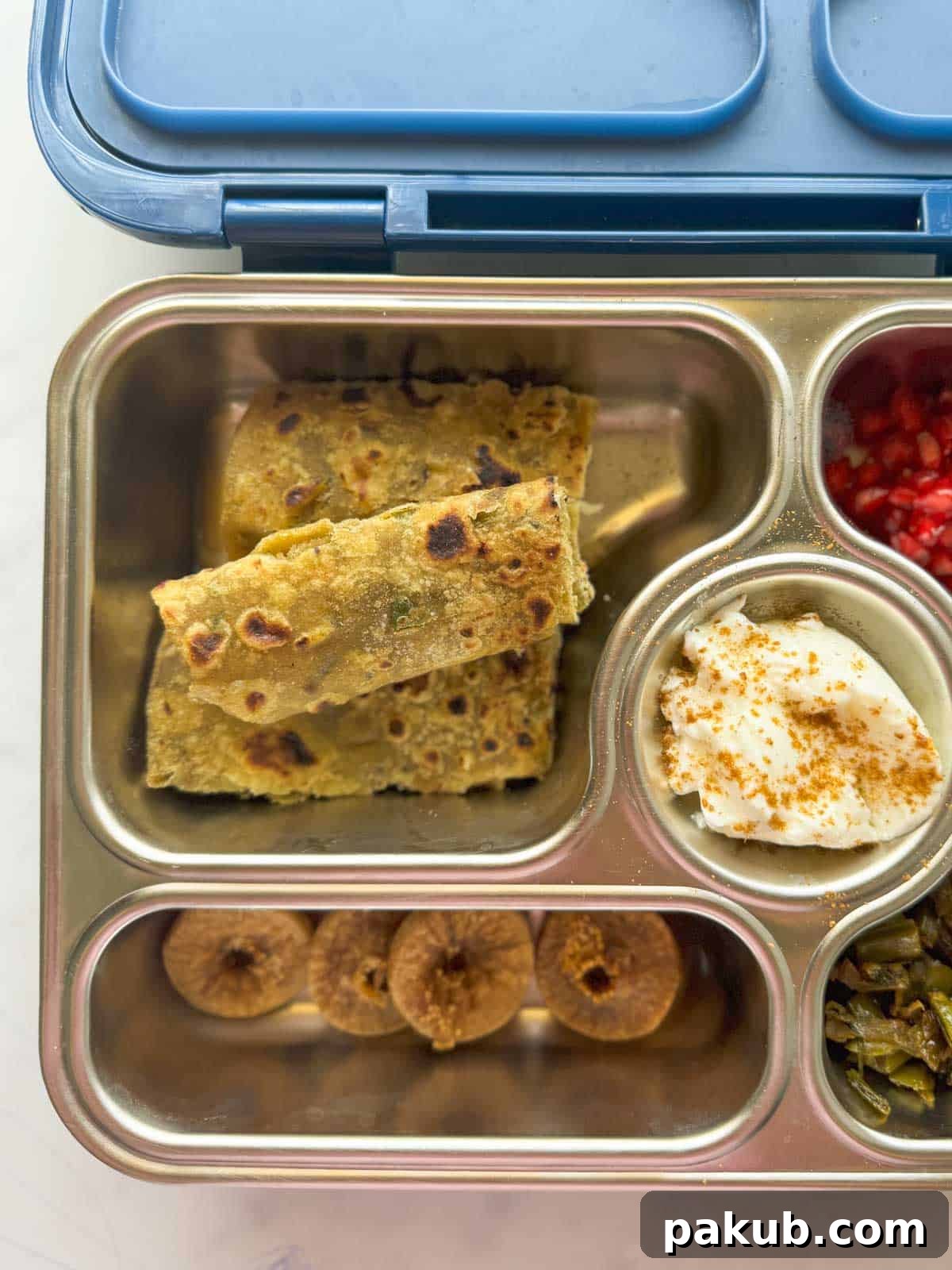 Spiced Lentil and Chutney Paratha 3 Dal paratha served in a kids tiffin box alongside fresh fruits, nuts, yogurt, and chopped vegetables, showcasing a balanced meal.