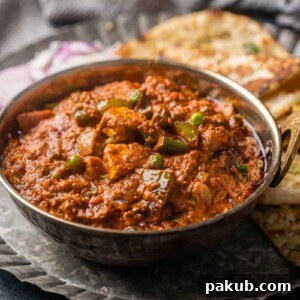 A vibrant picture of Veg Kolhapuri served in a traditional copper kadhai, resting on a plate with onions and naan.