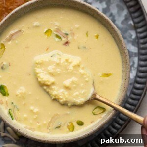 A close-up shot of a spoon revealing the creamy, layered texture of instant Rabdi in a rustic brown bowl.