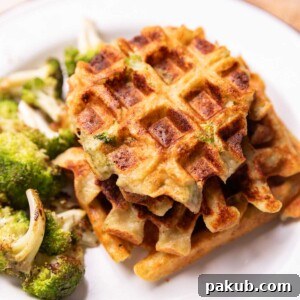 Broccoli cheese waffles served on a white plate with a side of roasted broccoli and a dollop of sour cream, garnished with fresh herbs
