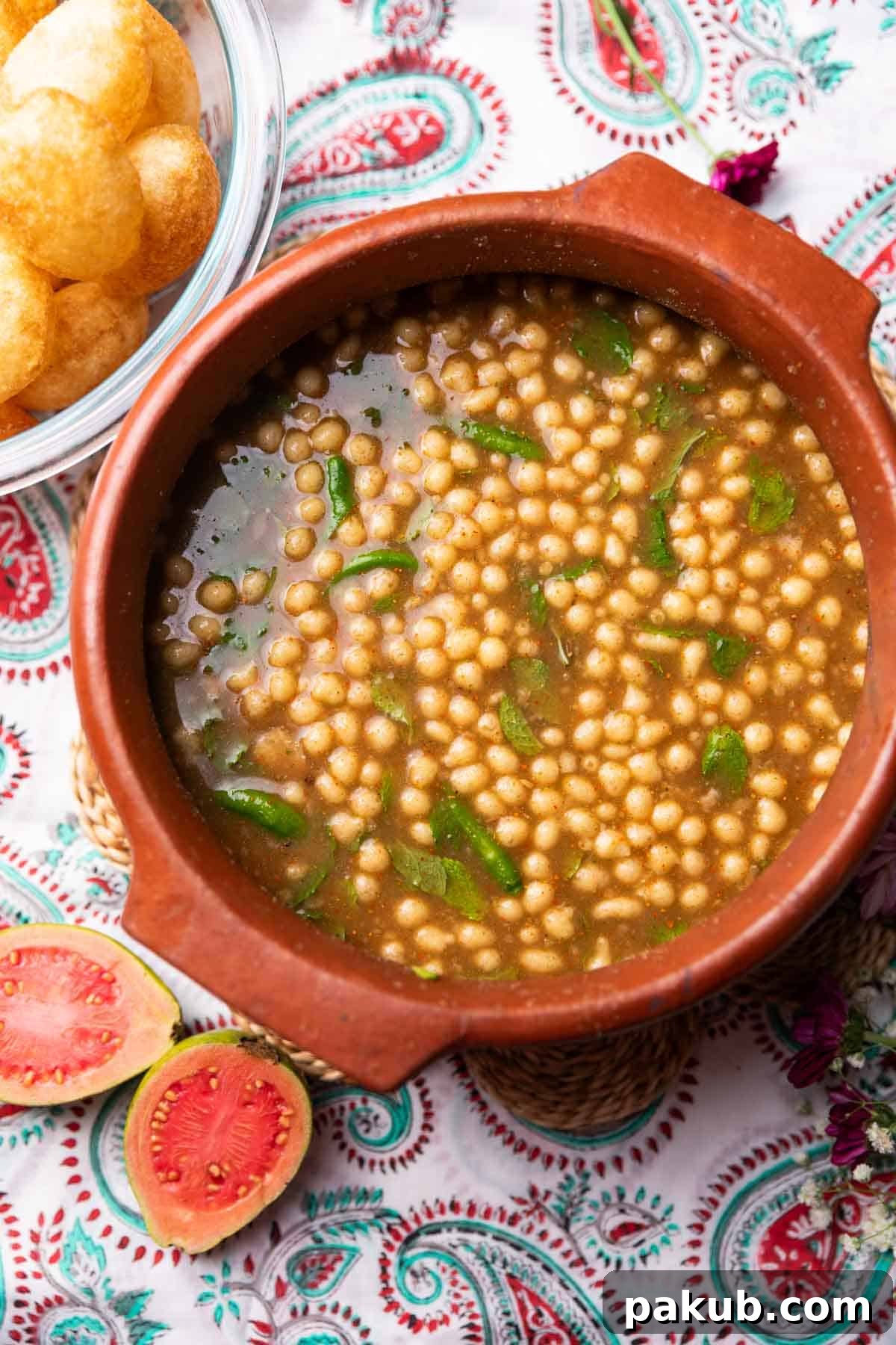 Close-up of a single Guava Pani Puri being dipped into a bowl of guava-infused water, garnished with boondi