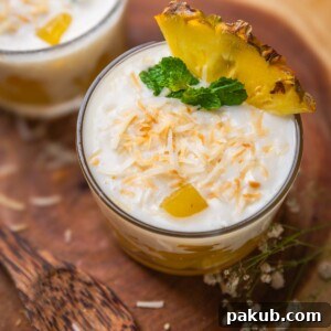 coconut pudding with pineapple jelly garnished with toasted coconut flakes, pineapple slice and mint leaves and served in shot glasses