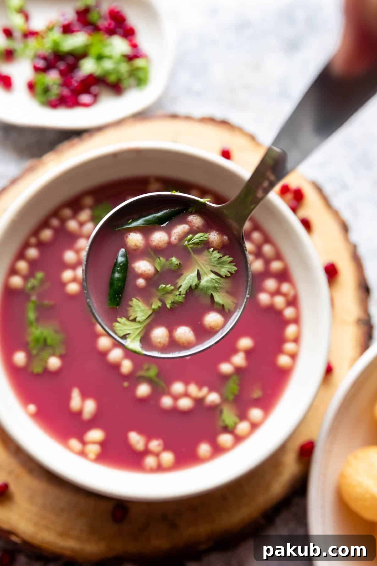 Ruby Red Pani Puri 3 Close-up shot of Anar Pani Puri garnished with coriander leaves and boondi, served in a white bowl with a small ladle, highlighting its readiness for a delicious bite.