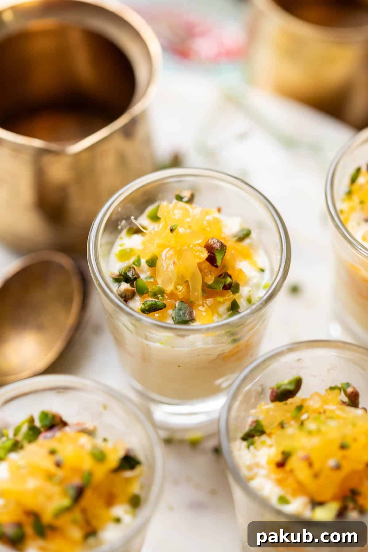 Vibrant Orange Kalakand 3 A close-up view of Orange Kalakand in shot glasses, showcasing the creamy layers, orange segments, and chopped pistachios.