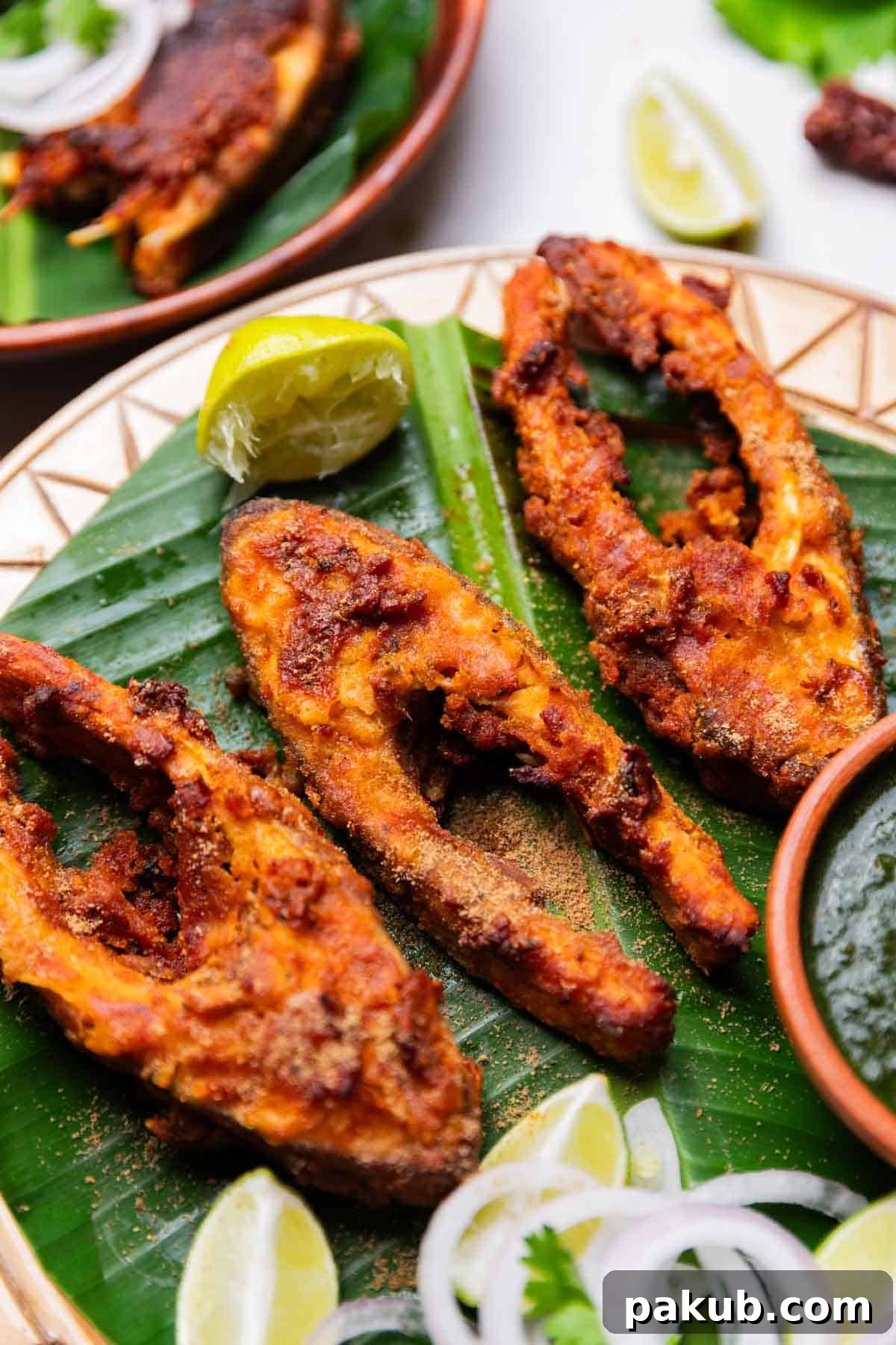 A close-up view of perfectly air-fried Amritsari fish fry pieces arranged beautifully on a green leaf platter, garnished with fresh cilantro and served alongside green chutney for dipping.