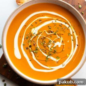 A beautifully presented bowl of Roasted Pumpkin Pepper Soup, garnished with a generous swirl of cream and crushed pistachios, perfectly paired with slices of buttered crusty bread on the side.
