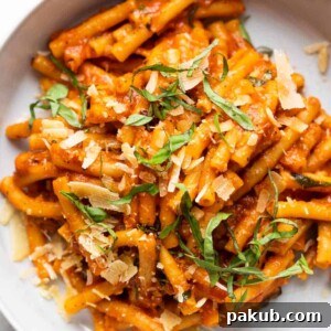 Pasta in red sauce, elegantly topped with shaved Parmesan and fresh basil, served in a stylish grey-white bowl with a fork on the side