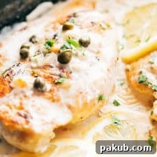 A close-up of creamy lemon chicken scallopini, garnished with bright lemon slices and briny capers on top