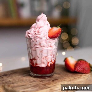 Elegant strawberry mousse layered in a glass with strawberry compote, gracefully topped with half a fresh strawberry on a wooden board