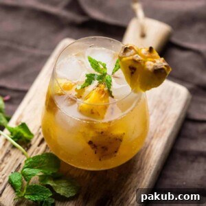 A unique Roasted Pineapple Moscow Mule served in a stemless wine glass, garnished with fresh mint sprigs