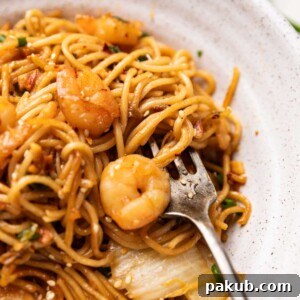 A close-up of vibrant chili garlic prawn noodles, beautifully served in a white bowl with a fork ready to enjoy