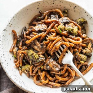 Thick Black Pepper Udon Noodles served beautifully in a white bowl with a fork, ready to be enjoyed