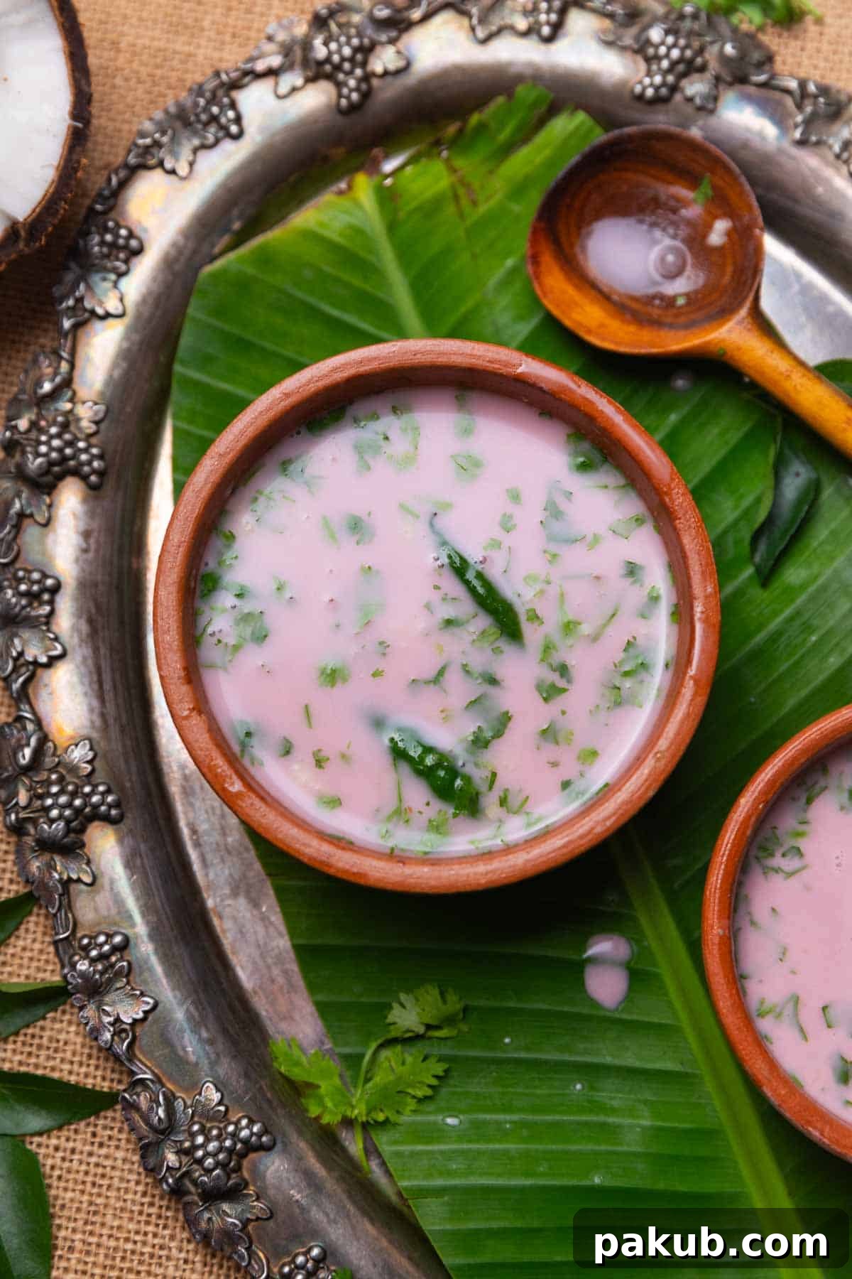 Small earthen bowls filled with Sol Kadhi, each garnished with fresh coriander and a green chili, arranged on a rustic table.