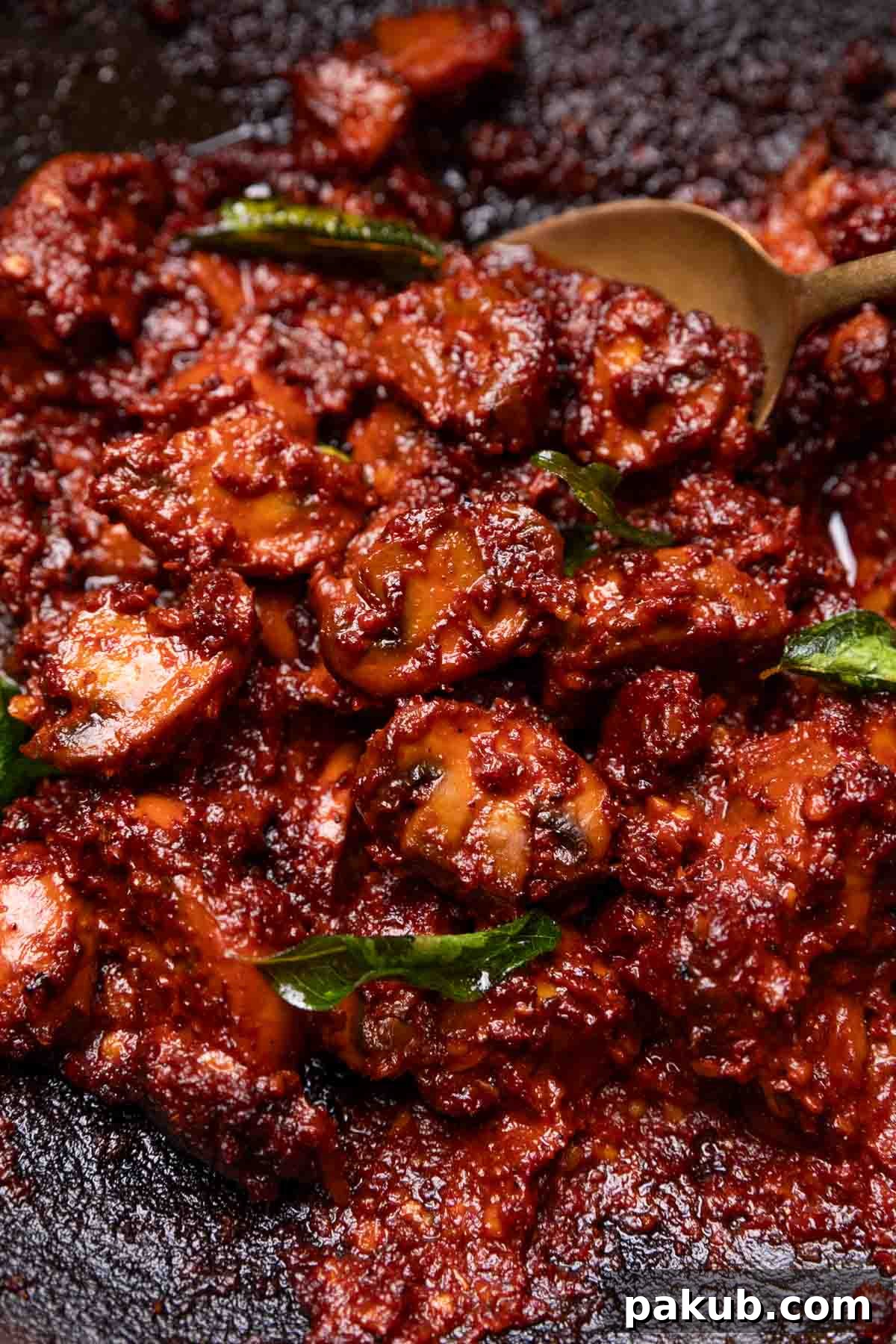Close-up image of rich, dark red Mushroom Ghee Roast simmering in a pan, highlighting the glossy texture and aromatic masala