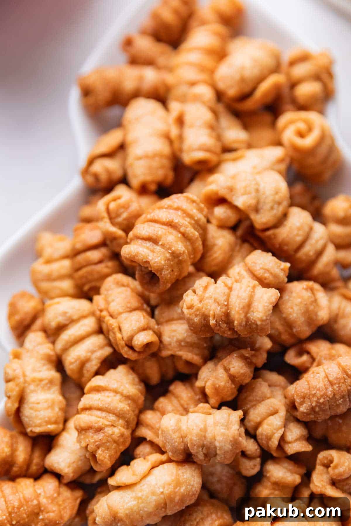 A close-up shot of several Kulkuls on a white background, highlighting their intricate curled shape and golden, crispy texture. The details of the pastry's flaky layers are visible.