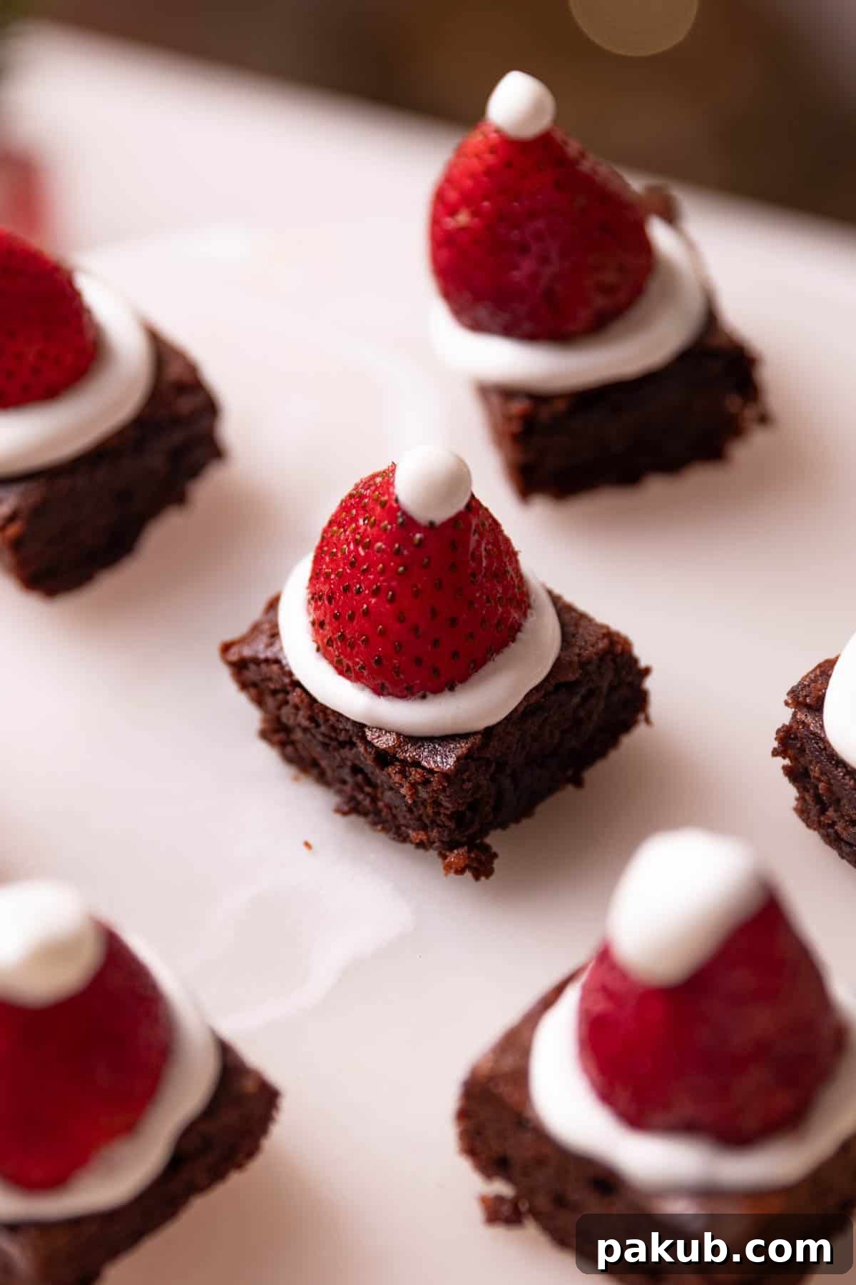 A large white serving platter artfully arranged with numerous brownie bites, each topped with white frosting and a fresh strawberry, beautifully showcasing them as an ideal dessert for any celebratory occasion.