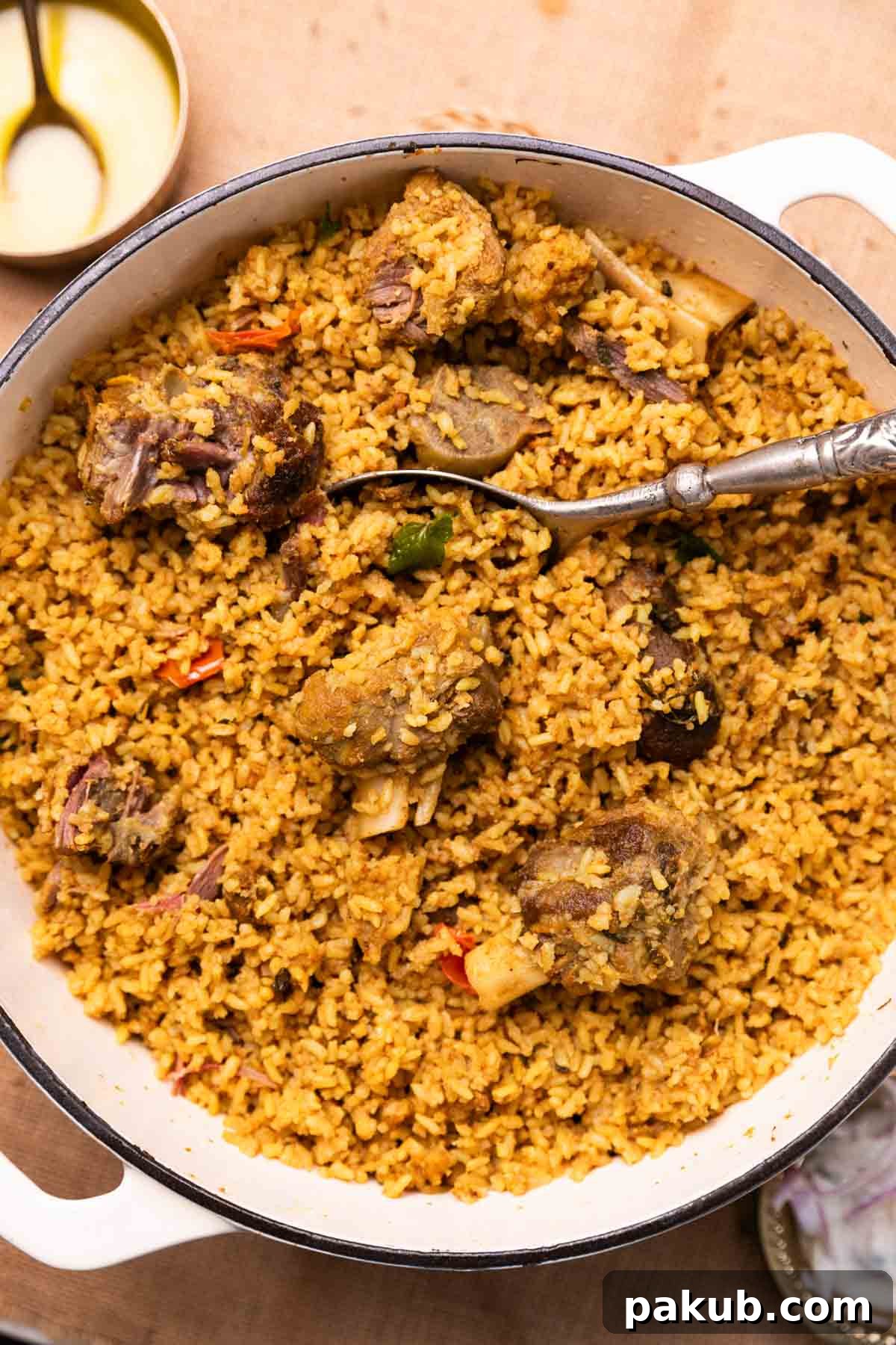 Rich, dark brown Dindigul style mutton biryani served in a traditional metal pan with a spoon, ready to be enjoyed.