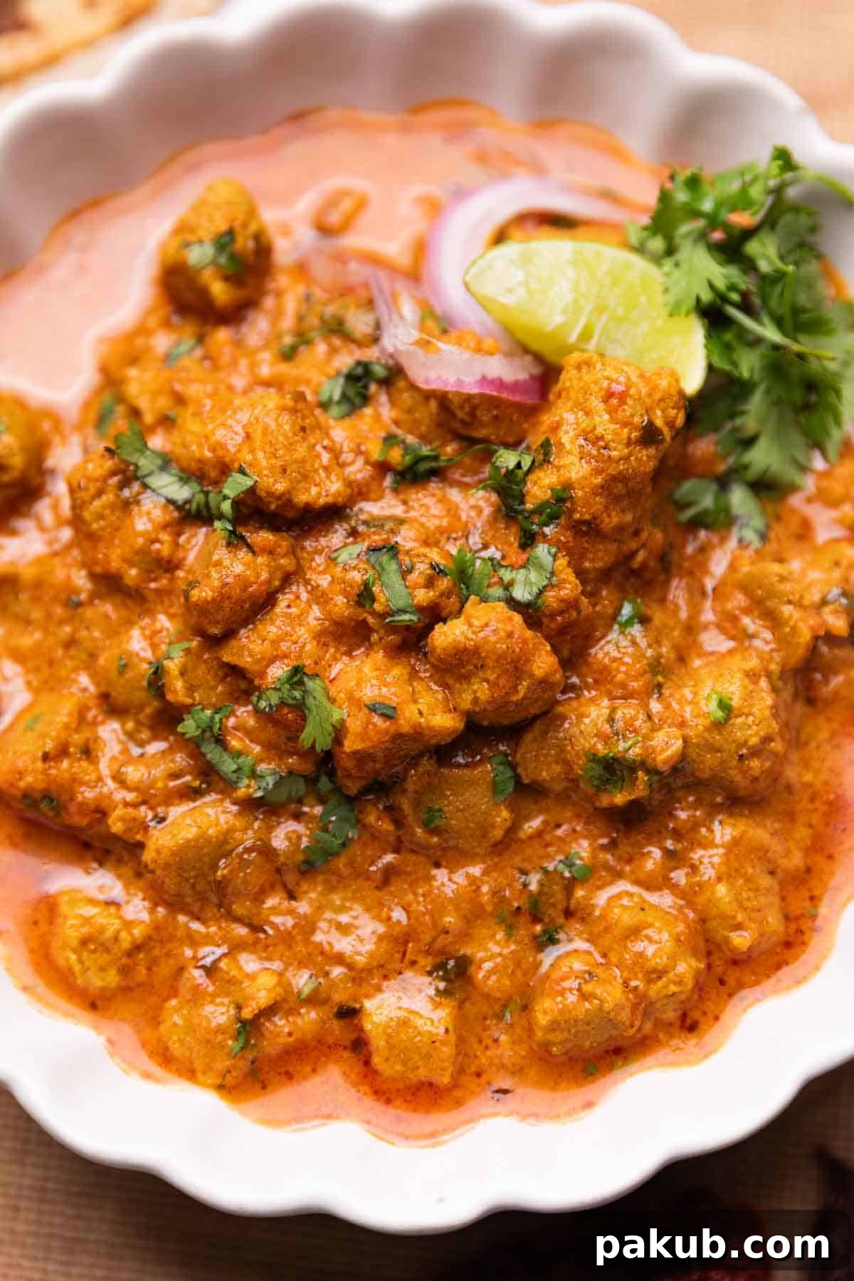 Savory Soya Nugget Curry 2 Delicious soya curry served in a bowl, garnished with fresh onion, a lemon wedge, and vibrant coriander leaves, ready to be enjoyed.