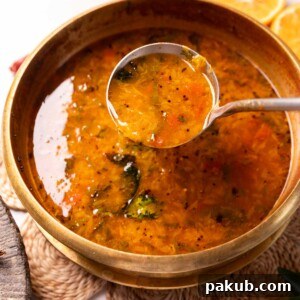 Orange rasam in a container with a ladle, ready to be served, highlighting its vibrant color.