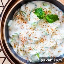 Indian Spiralized Cucumber Mint Raita garnished with some mint, masala and served in a black bowl.