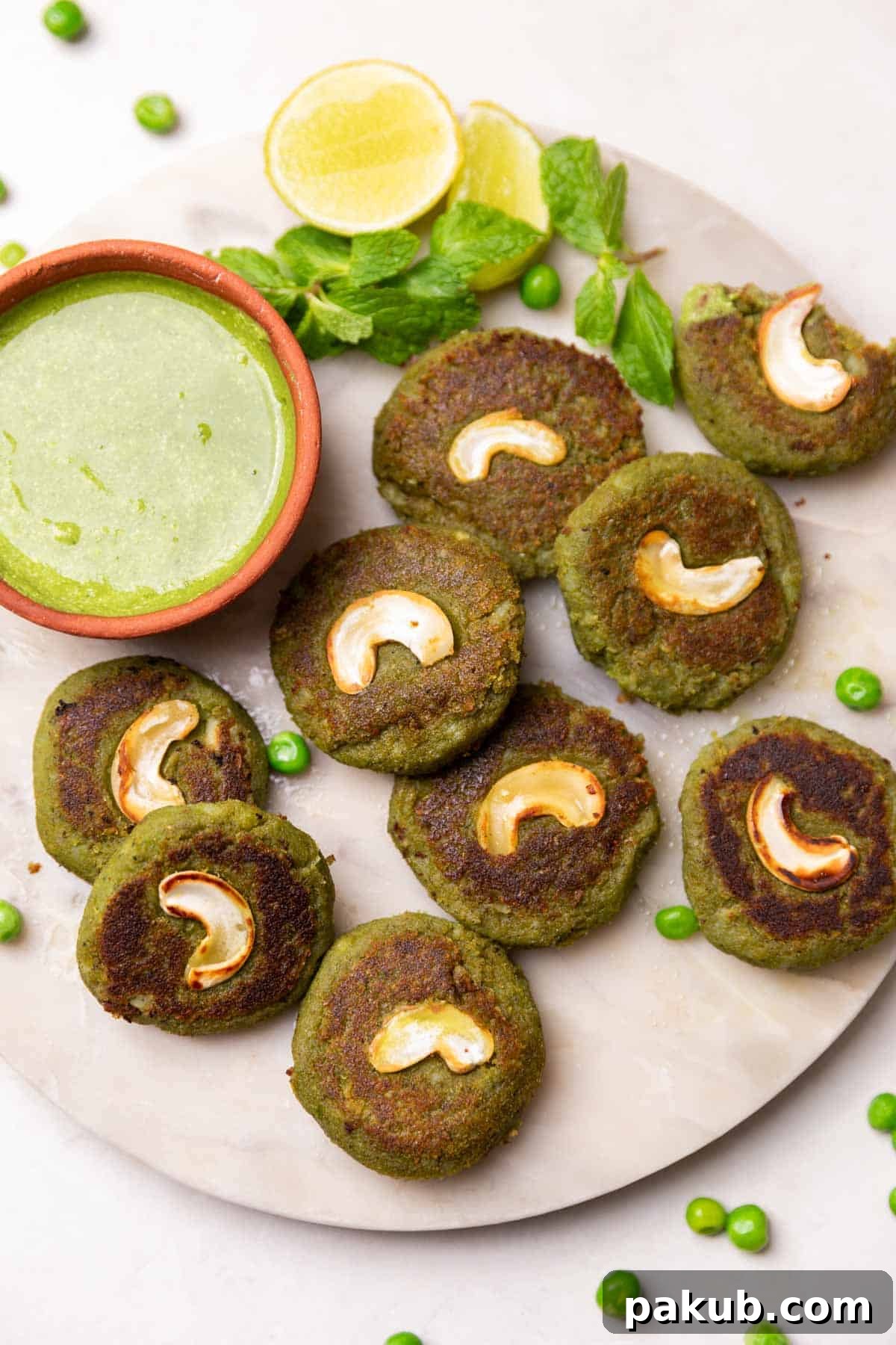 Emerald Vegetable Kebab 2 Vibrant green Hara Bhara Kebabs served on a white round platter with a side of fresh green chutney and lemon wedges, showcasing their crispy exterior.