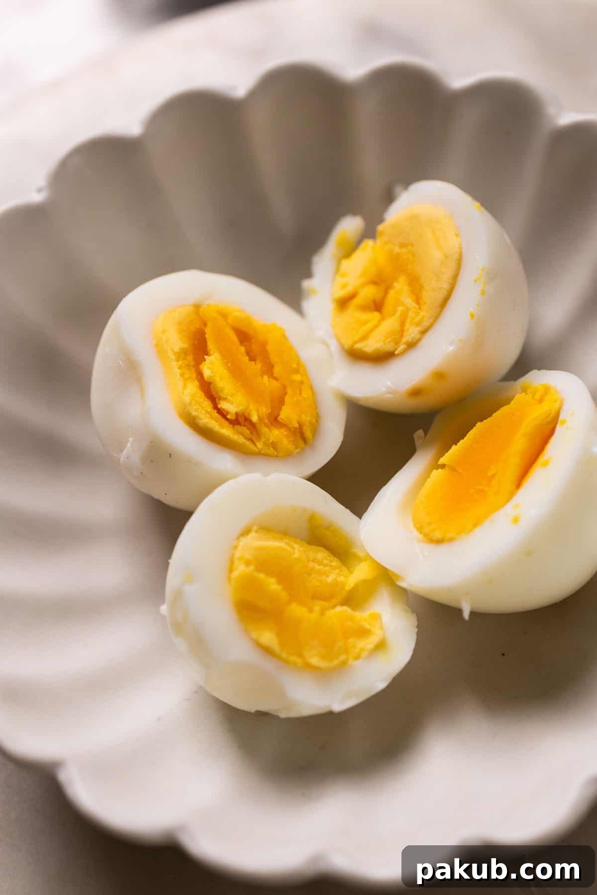 No-Boil Air Fryer Eggs 3 Half-cut hard-boiled air fryer eggs in a white bowl, showing perfectly cooked yolks.