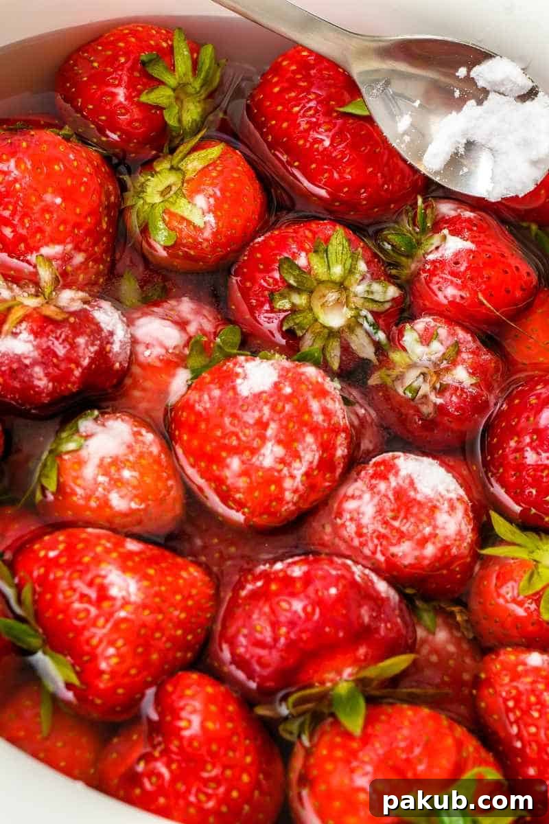 Simple Steps to Perfectly Clean Berries 3 A close-up image of vibrant red strawberries gently soaking in a water solution with a sprinkling of baking soda, illustrating the cleaning process.
