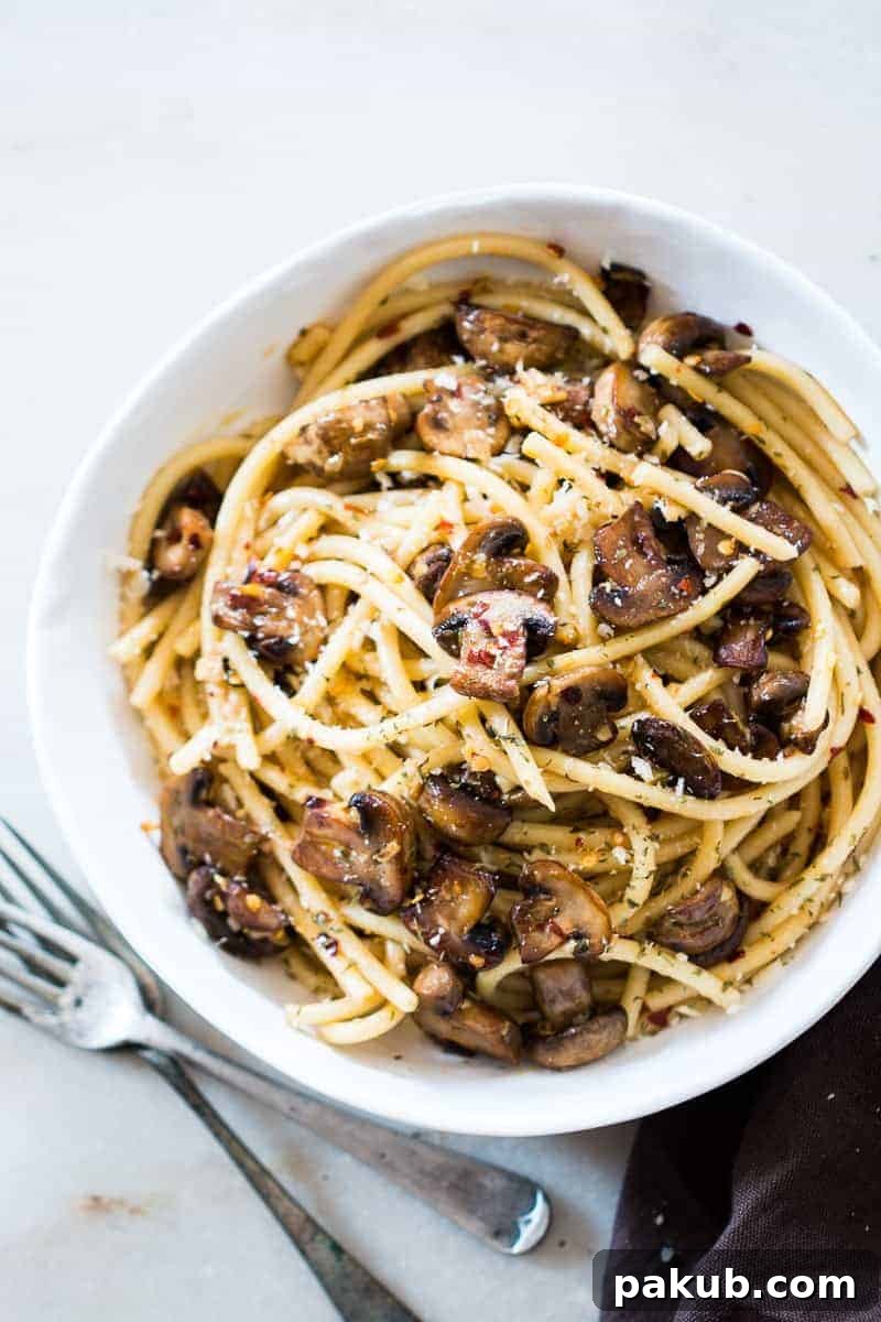 A close-up shot of freshly prepared Mushroom Spaghetti Aglio Olio, garnished with green parsley and a sprinkle of Parmesan cheese, ready to be served in a rustic bowl on a wooden surface.