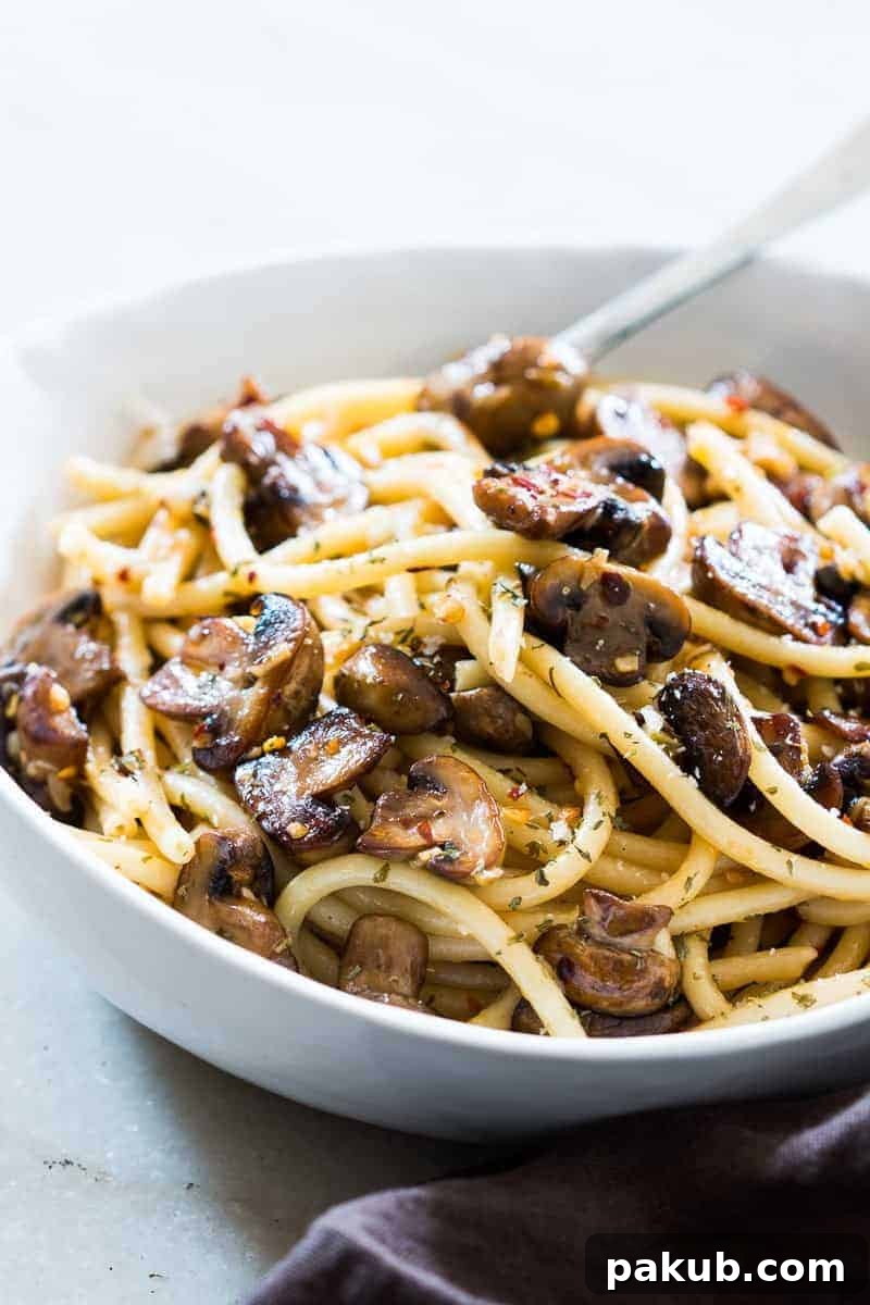 A vibrant bowl of Mushroom Spaghetti Aglio Olio topped with fresh parsley and grated Parmesan cheese, showcasing the golden-brown mushrooms and perfectly cooked pasta.