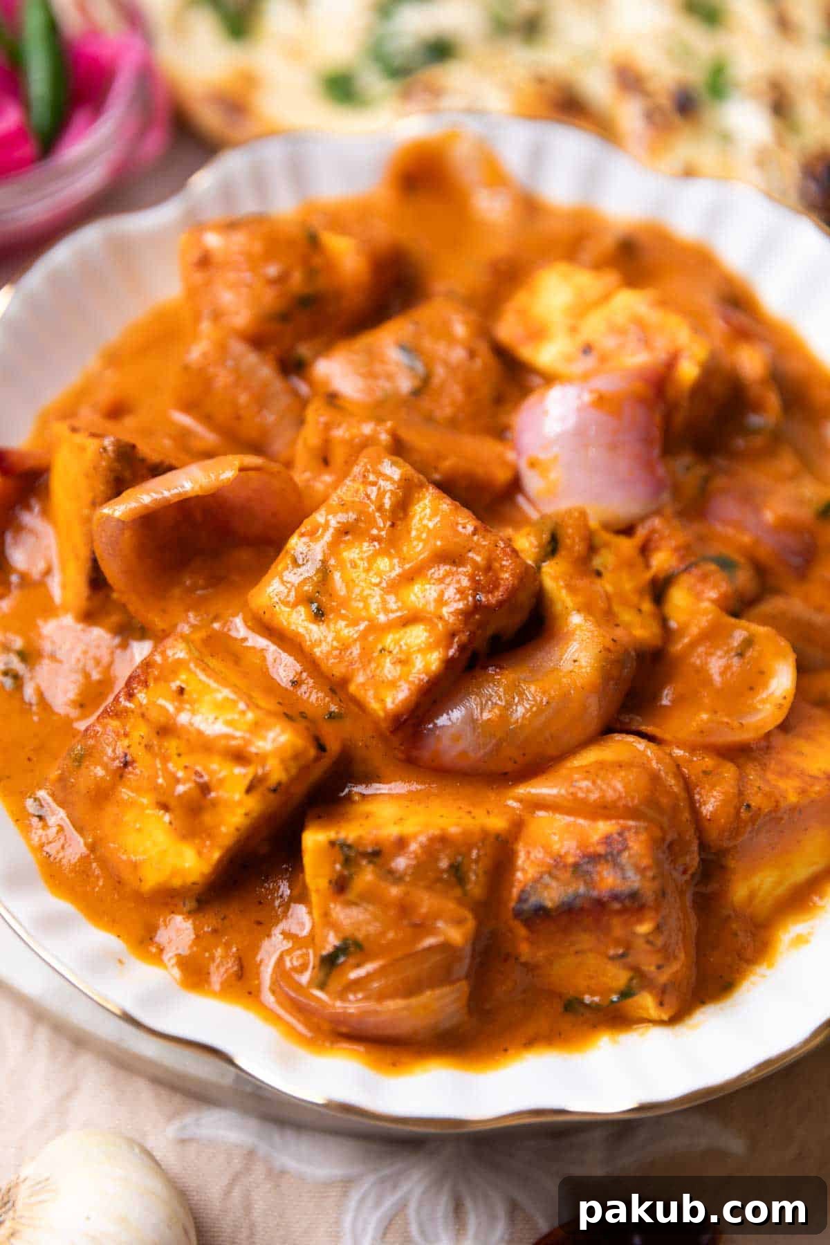Vibrant Paneer Do Pyaza curry served in a white bowl, garnished with fresh cilantro, with warm Indian bread and rice in the background.