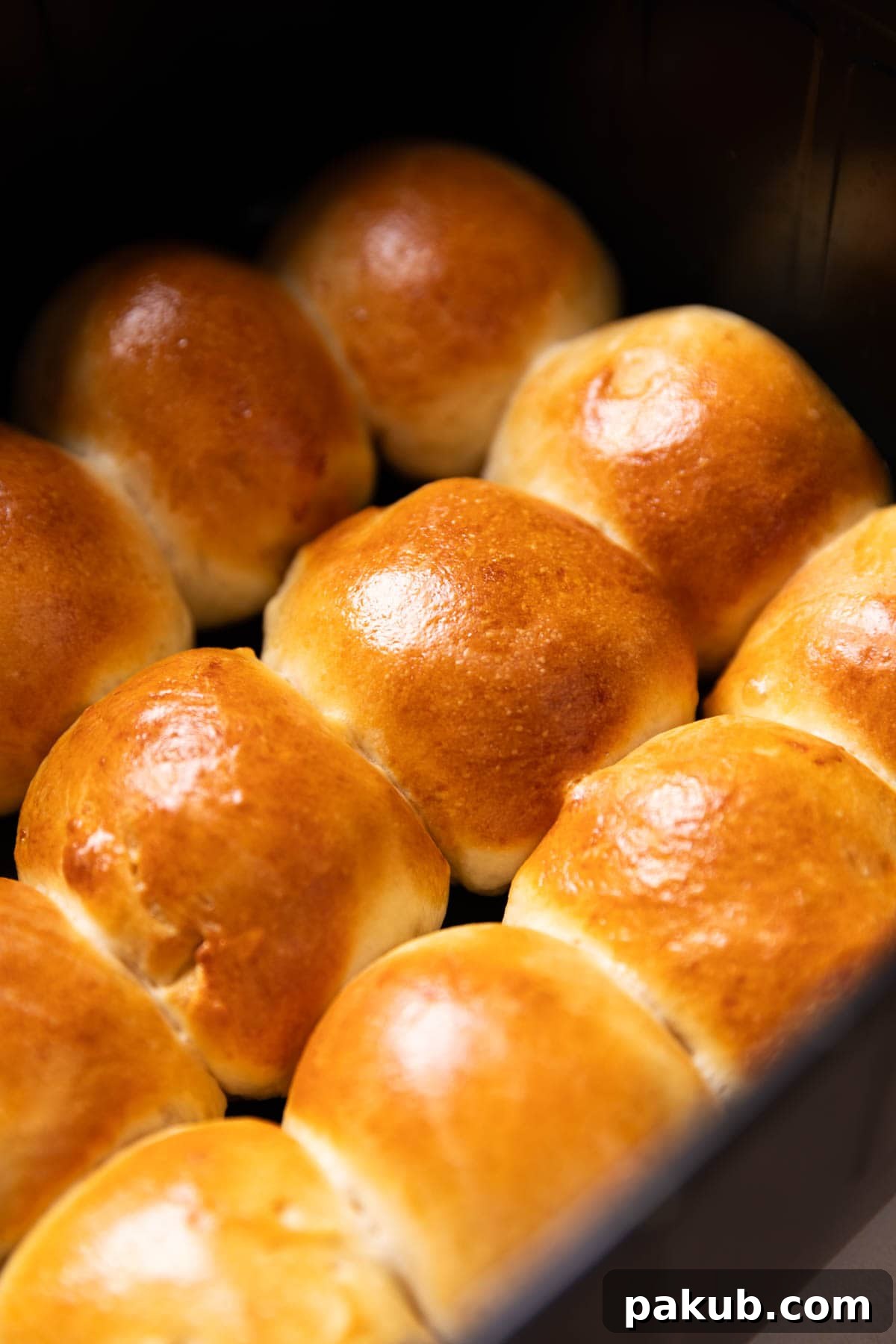 Effortless Air Fryer Dinner Rolls 3 Freshly baked air fryer dinner rolls glistening with melted butter and sprinkled with fragrant sesame and kalonji seeds, cooling in the air fryer basket after achieving golden perfection.