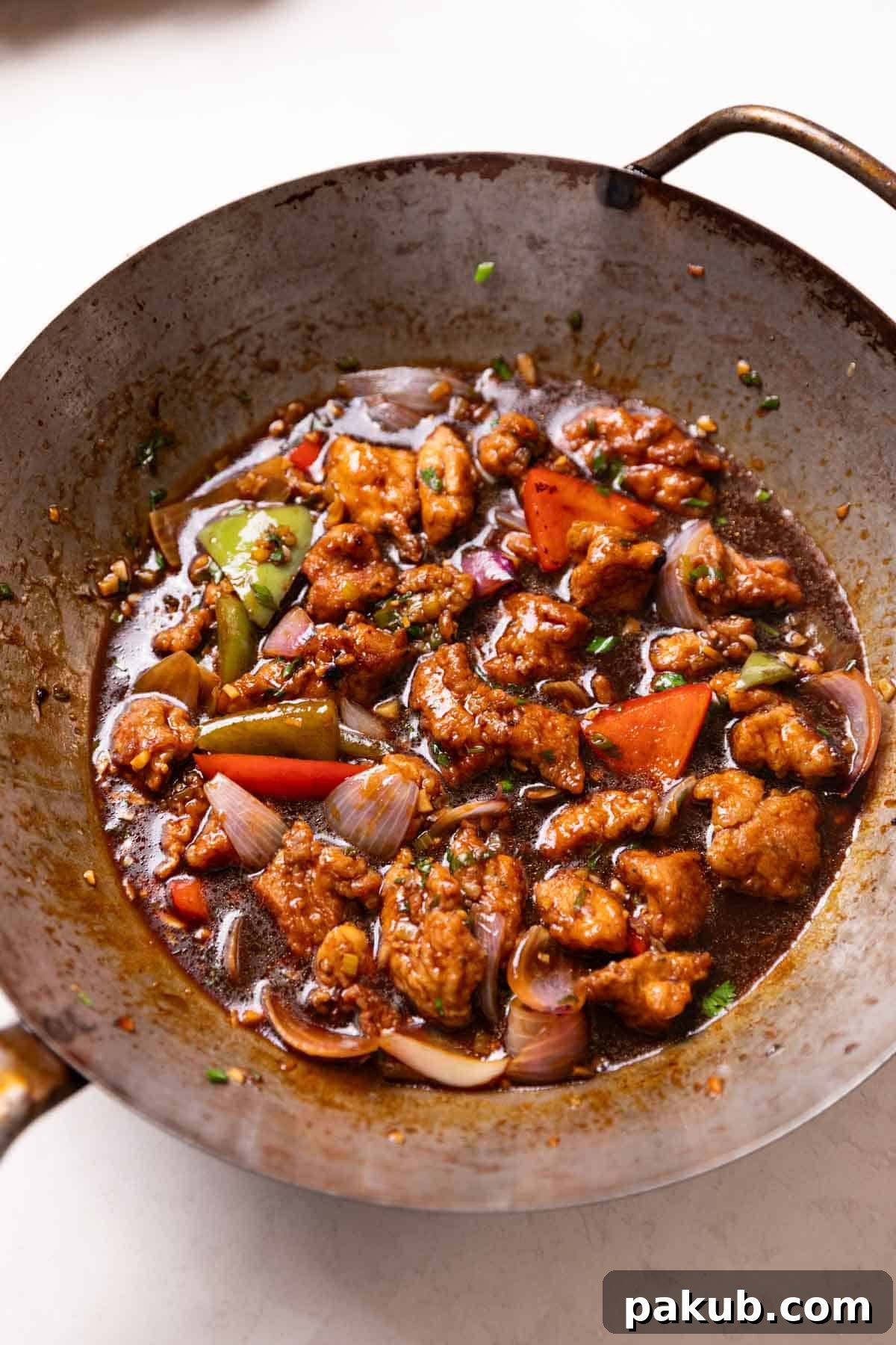 Freshly cooked Chicken Manchurian glistening in a wok, garnished with spring onions, ready to be transferred to a serving dish.