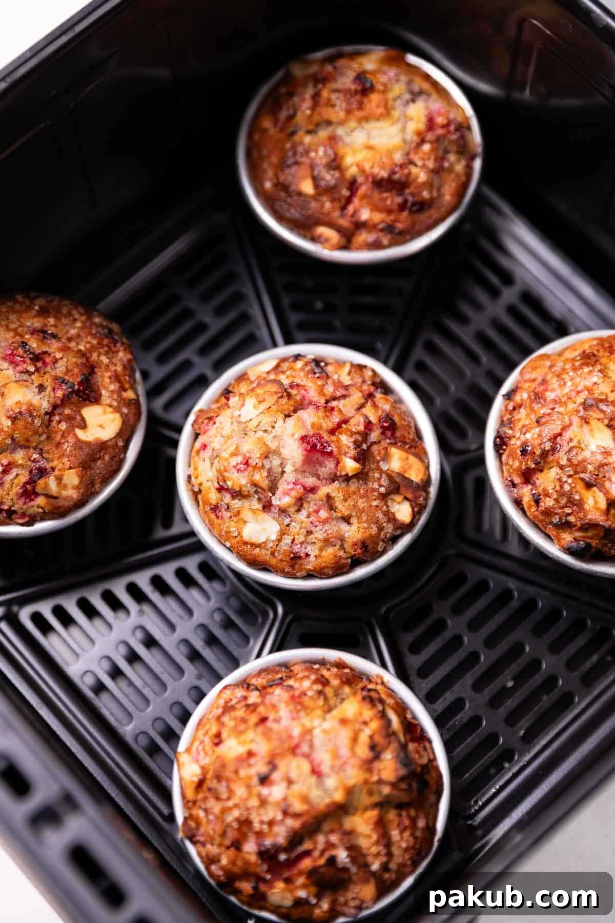 Air Frying Demystified 3 freshly baked strawberry muffins arranged on a plate next to an air fryer