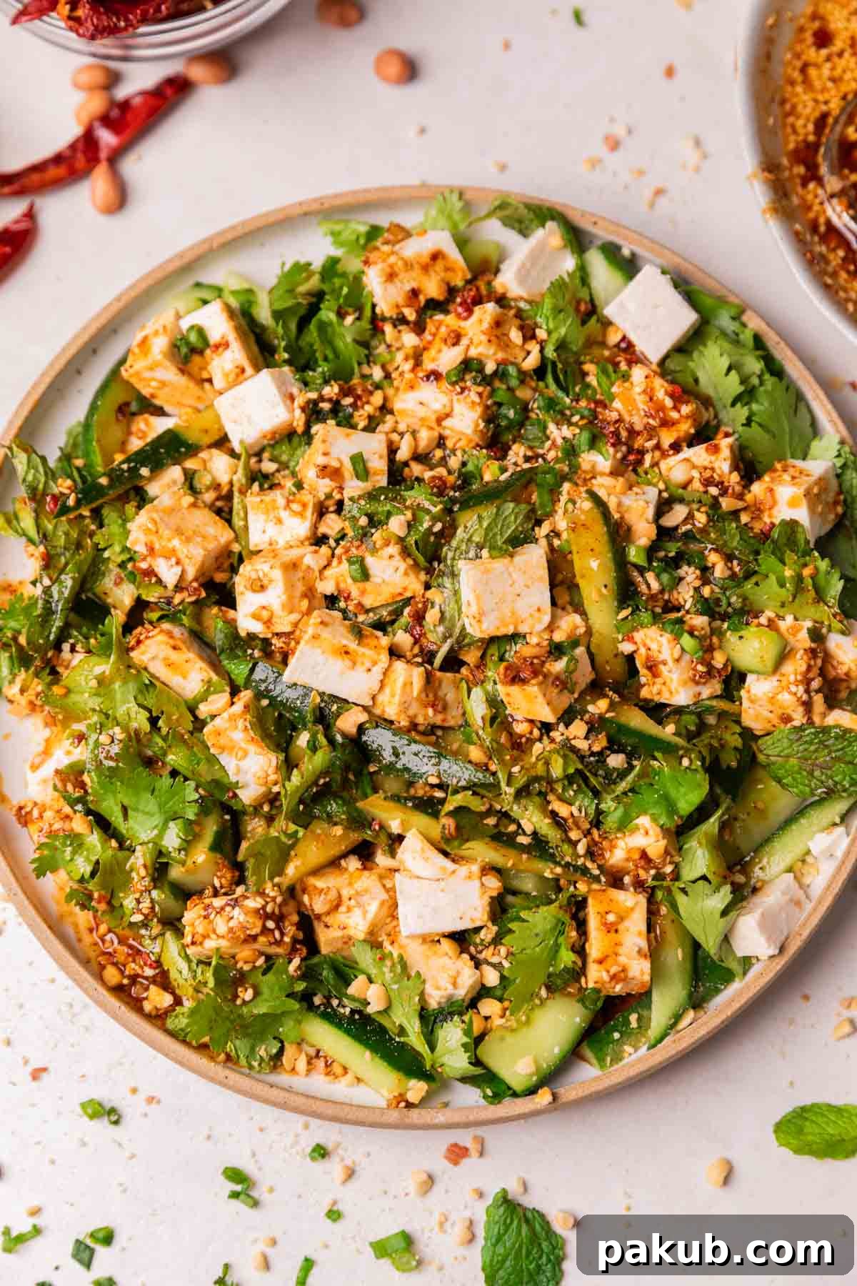 Zesty Sesame Tofu and Cucumber Salad 2 A vibrant Asian cucumber salad with tofu, sprinkled with peanuts and herbs, served on a white platter, ready to be enjoyed.