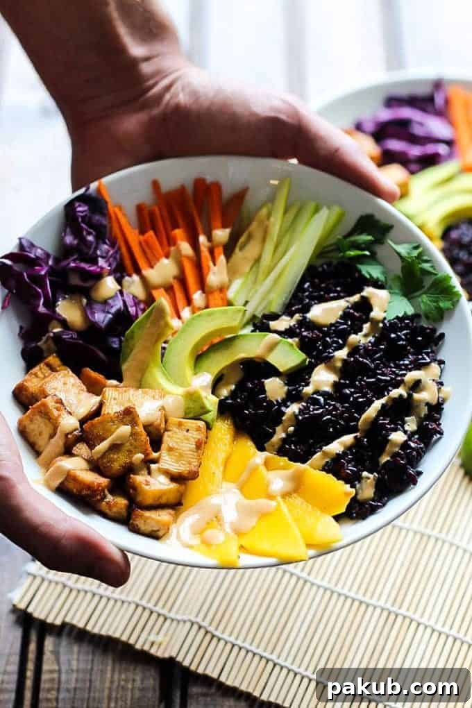 A collection of 13 insanely delicious savoury mango recipes that are sure to blow your mind if you've always had mangoes in sweet dishes. These recipes combine the juicy sweetness of mangoes with savoury ingredients to create a dish that's truly stellar and unforgettable! #spring #mango #recipes #easter #summer #fruit A hand holding a vibrant Tofu and forbidden rice bowl, showcasing the colorful and healthy ingredients within, perfect for a plant-based meal.