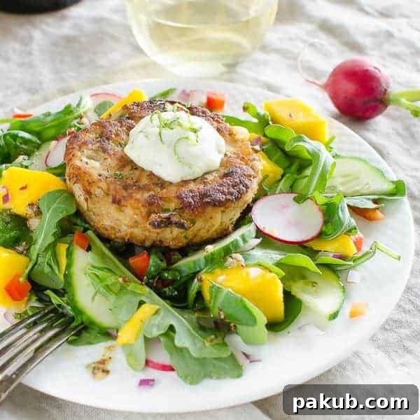 A collection of 13 insanely delicious savoury mango recipes that are sure to blow your mind if you've always had mangoes in sweet dishes. These recipes combine the juicy sweetness of mangoes with savoury ingredients to create a dish that's truly stellar and unforgettable! #spring #mango #recipes #easter #summer #fruit Gourmet mango crab cakes elegantly plated with a fresh mango lettuce salad, served on a white plate with a fork, ready to be savored.