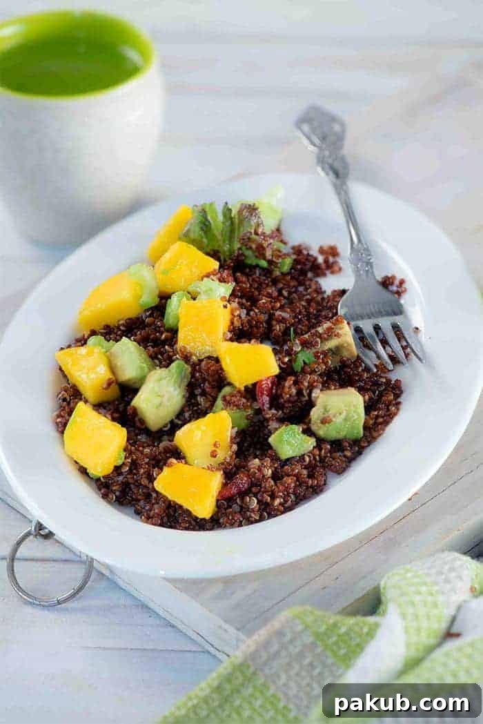 A collection of 13 insanely delicious savoury mango recipes that are sure to blow your mind if you've always had mangoes in sweet dishes. These recipes combine the juicy sweetness of mangoes with savoury ingredients to create a dish that's truly stellar and unforgettable! #spring #mango #recipes #easter #summer #fruit A colorful Red Quinoa Mango Salad presented in a deep white plate, accompanied by a fork and a refreshing glass of water.