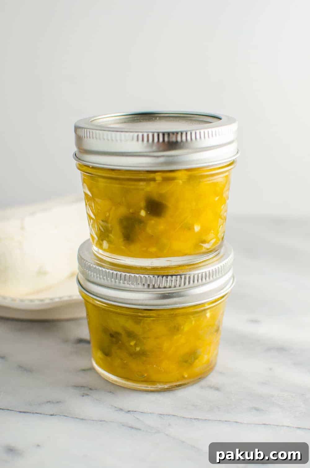 A collection of 13 insanely delicious savoury mango recipes that are sure to blow your mind if you've always had mangoes in sweet dishes. These recipes combine the juicy sweetness of mangoes with savoury ingredients to create a dish that's truly stellar and unforgettable! #spring #mango #recipes #easter #summer #fruit Two glass jars filled with homemade Mango Jalapeno Jam, neatly stacked one on top of the other, showcasing the rich color of the preserve.