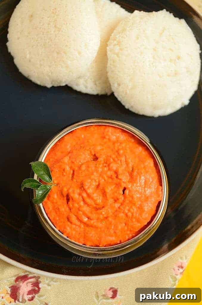 A collection of 13 insanely delicious savoury mango recipes that are sure to blow your mind if you've always had mangoes in sweet dishes. These recipes combine the juicy sweetness of mangoes with savoury ingredients to create a dish that's truly stellar and unforgettable! #spring #mango #recipes #easter #summer #fruit A vibrant reddish raw mango chutney, richly textured and served in a small bowl, accompanied by soft idlis, suggesting a traditional South Indian meal.