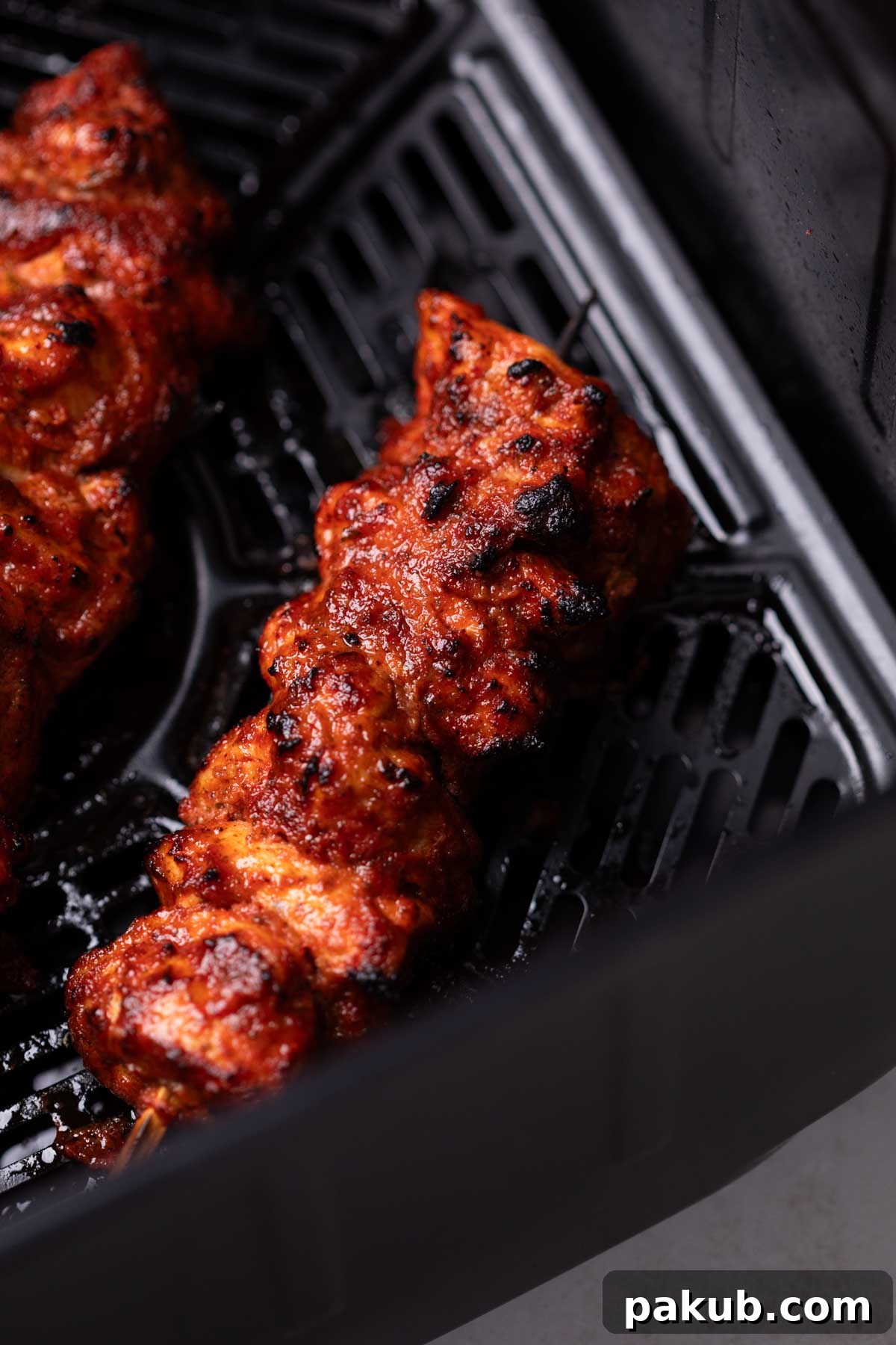 Close-up image of perfectly air-fried chicken tikka pieces in an air fryer basket, ready to be added to the gravy