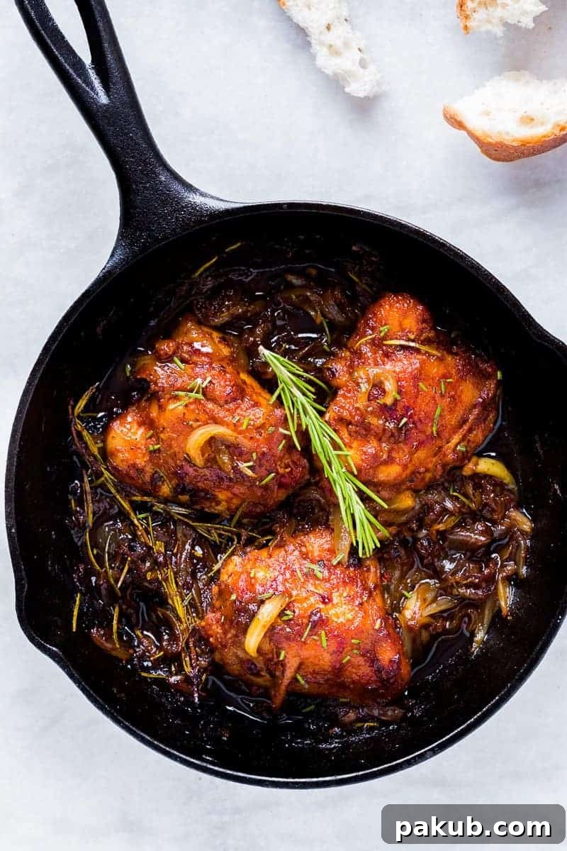 Close-up of golden caramelized onions and perfectly browned chicken thighs cooking in a cast iron skillet, highlighting the delicious texture and rich colors.