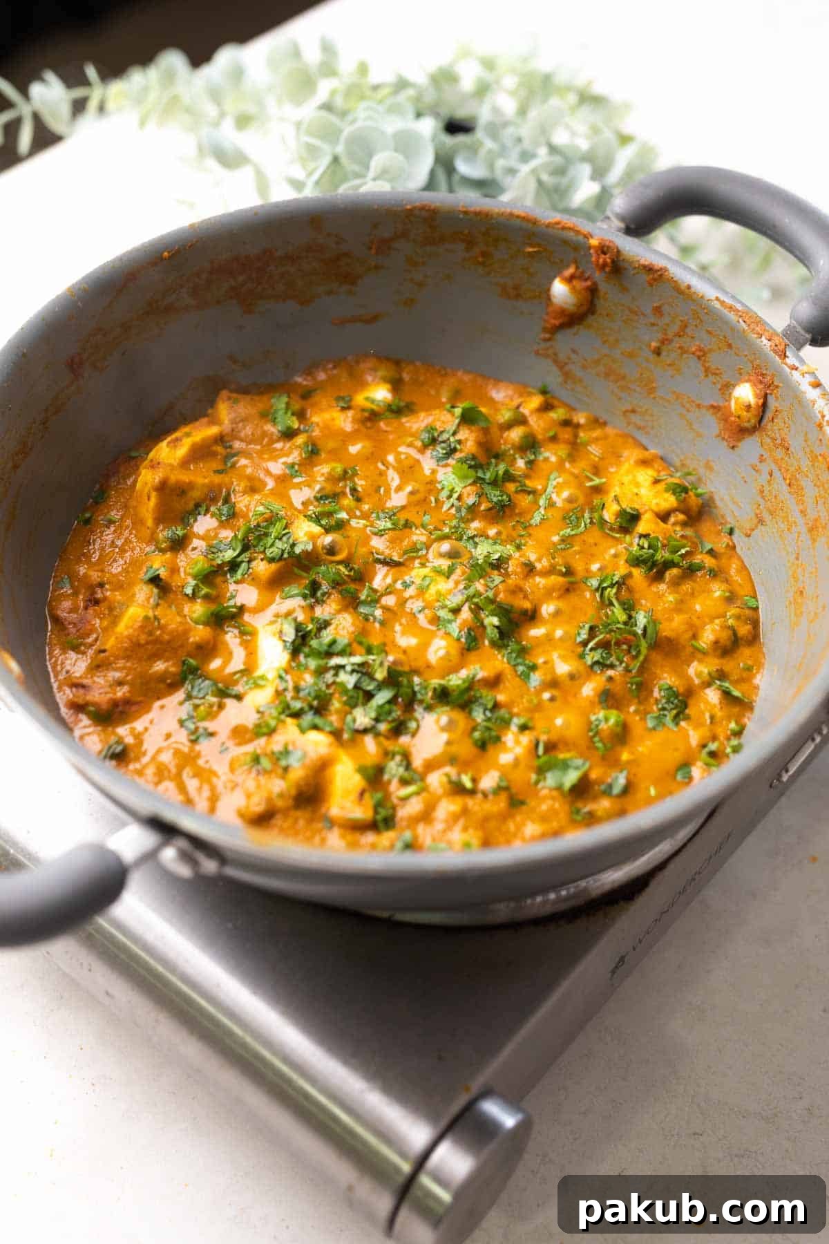 Velvety Matar Paneer Delight 5 A close-up shot of creamy Matar Paneer curry simmering in a gray pan, garnished with fresh coriander.