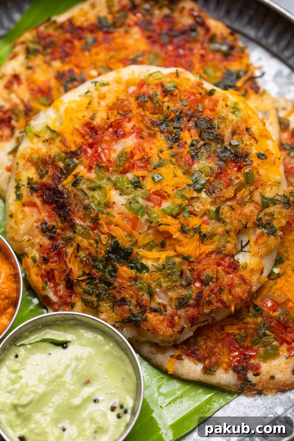 Your Go-To Recipe for Perfect Uttapam 3 Two vibrant Uttapams served on a banana leaf with an array of chutneys and sambar, ready to be enjoyed.