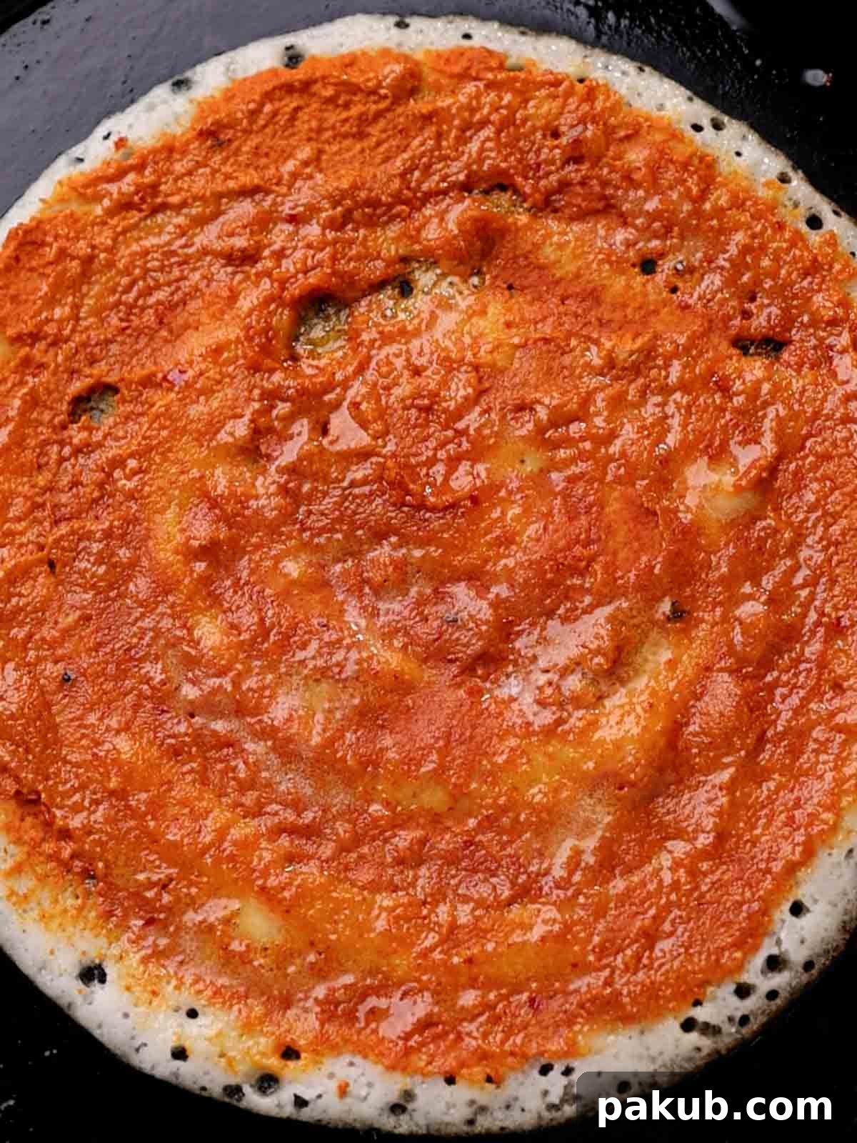 Red chutney spread on a mysore masala dosa on the pan