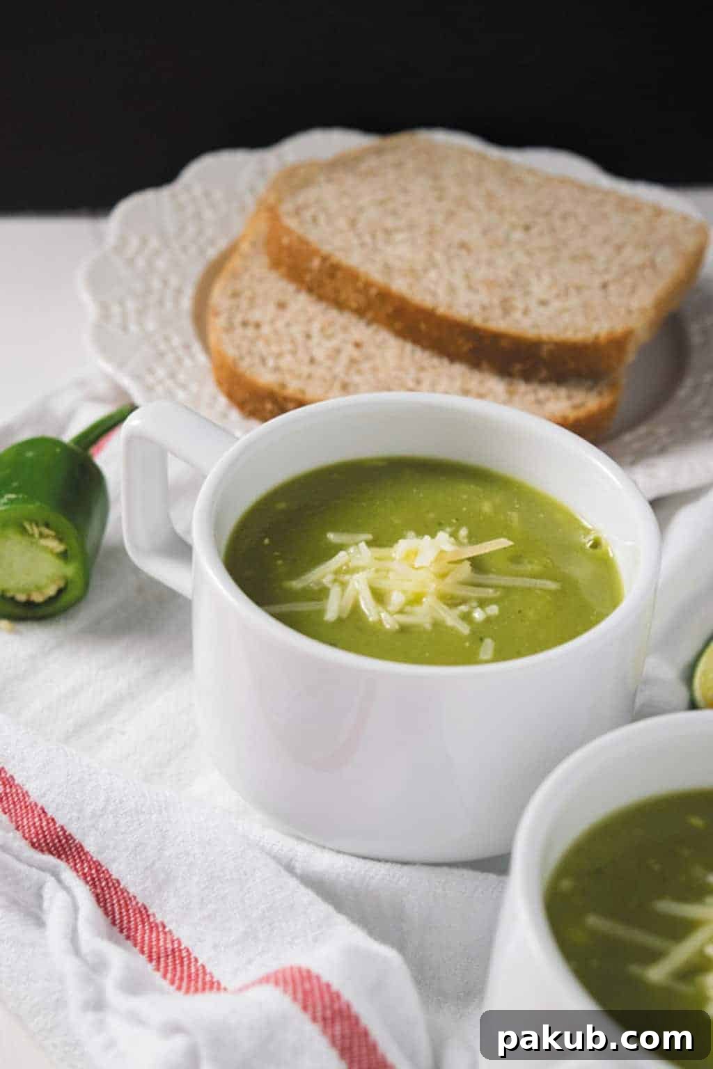 Zucchini Basil Soup Garnished Three white cups of pressure cooker zucchini basil soup, one garnished with shredded Parmesan and another with fresh basil, on a rustic wooden surface.