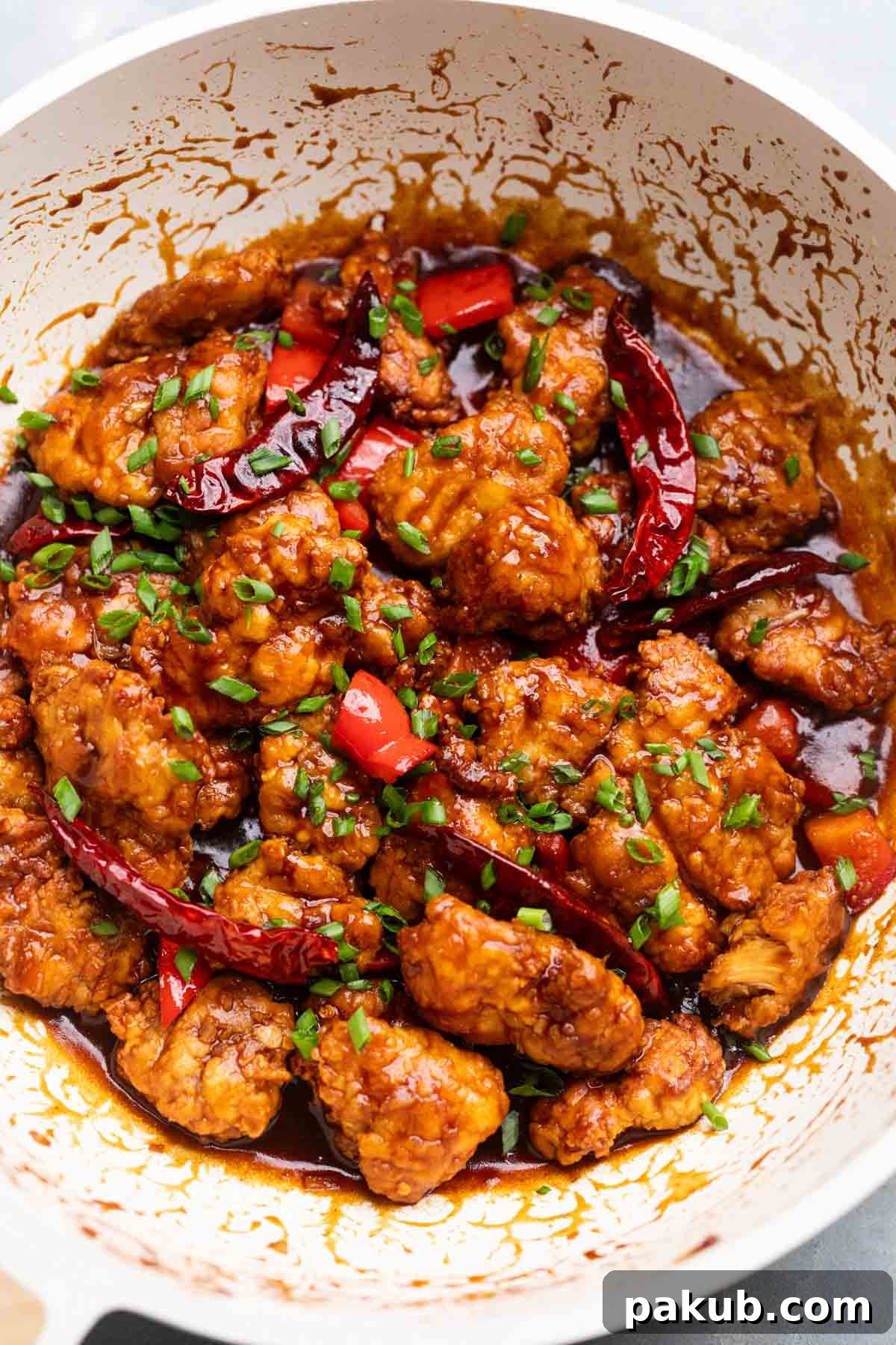 Freshly made air fryer General Tso's chicken, still warm in the frying pan, garnished with sesame seeds and spring onions, ready to serve