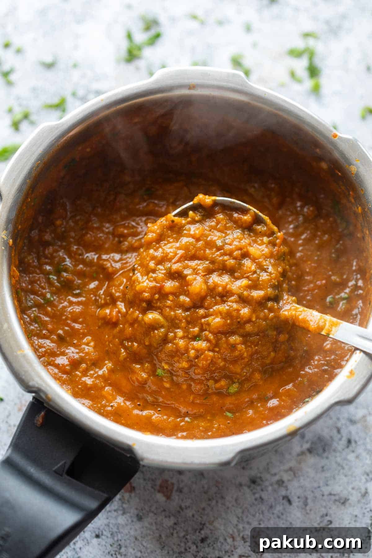 Close-up of freshly made one-pot pav bhaji being scooped up in a ladle, showcasing its rich texture and vibrant color.