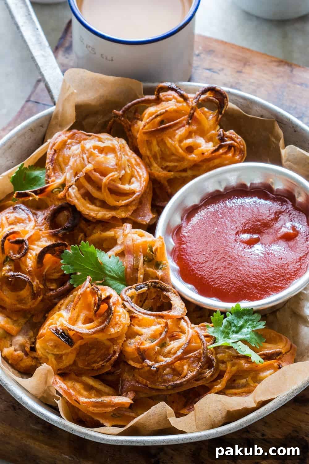 Crispy Baked Onion Pakodas (Fritters) – a healthier, guilt-free version of the popular Indian monsoon snack Kanda Bhaji, served with a cup of masala chai. These oven-baked fritters are incredibly crispy and can be made with various vegetables like potato, corn, or paneer.