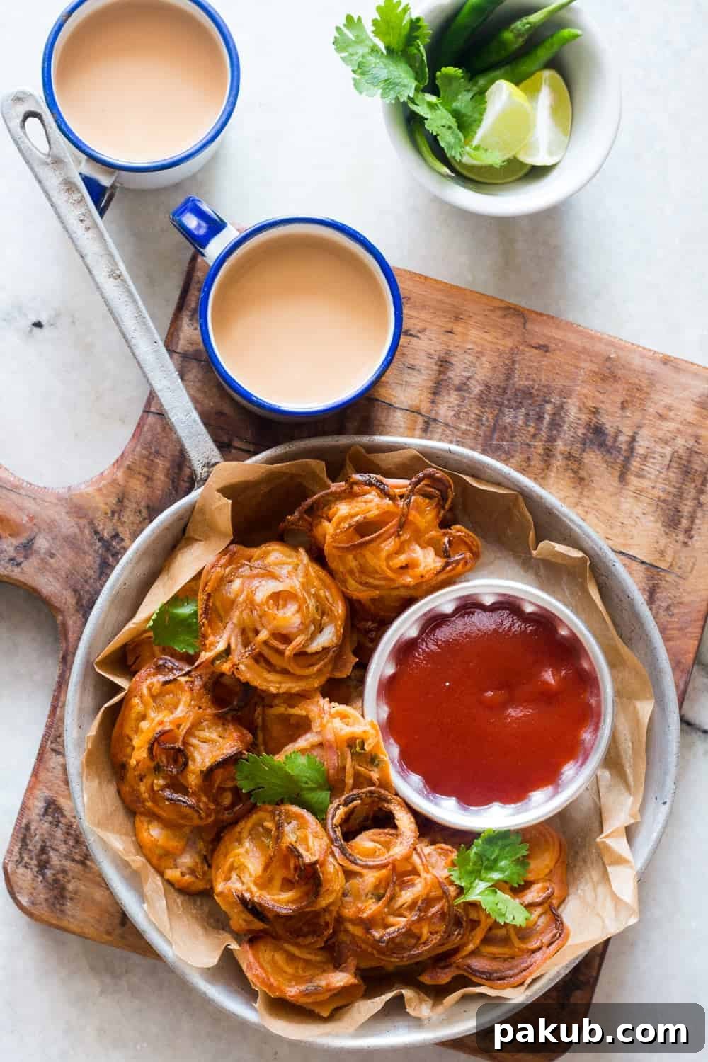 A vibrant plate of crispy baked onion pakodas (fritters) paired with fresh coriander chutney and a cup of traditional masala chai, perfect for a cozy Indian snack.