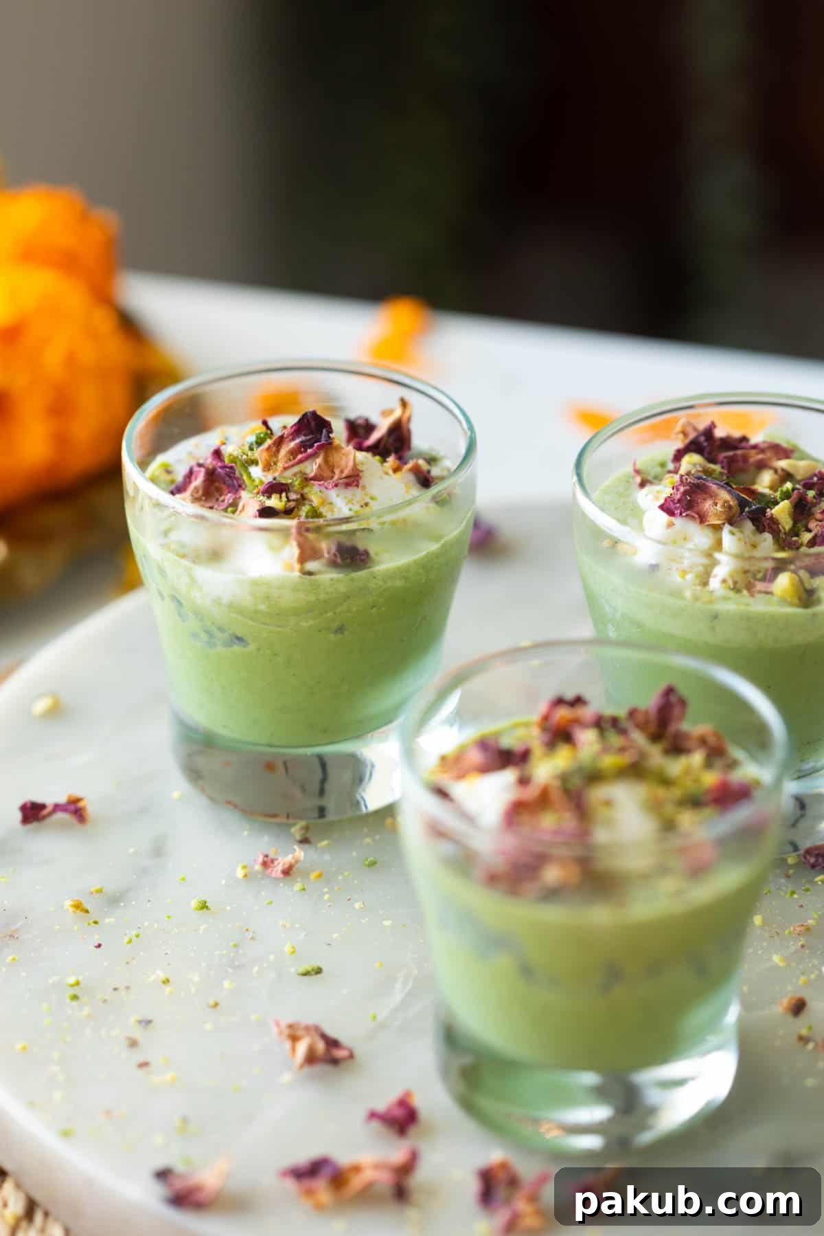 Close-up of vibrant green Falooda Paan Shots topped with creamy vanilla ice cream, delicate rose petals, and crunchy crushed pistachios